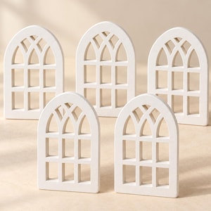 May include: Five identical white wooden window frame cutouts arranged in a group. Each piece features an arched top with a grid pattern consisting of three vertical sections and two horizontal bars, creating a classic window pane design.