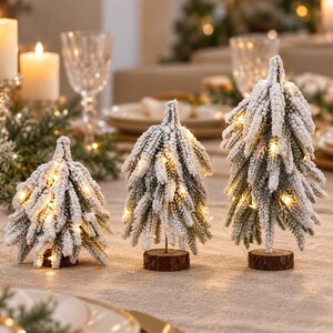 以下が含まれることがあります： 雪をかぶった緑の針葉と温かみのある白色LEDストリングライトが組み込まれた、3つのミニチュア人工クリスマスツリー。各ツリーは小さな丸い天然木の土台に取り付けられており、テーブルトップの装飾として使用されます。