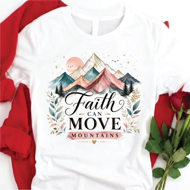 May include: A white t-shirt featuring a graphic of colorful mountains, pine trees, and a sun. The text "Faith CAN MOVE MOUNTAINS" is printed in black and pink lettering in the center, surrounded by delicate botanical illustrations and stars.