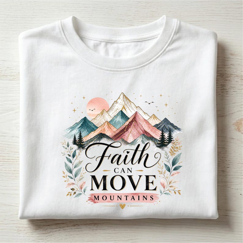May include: A white t-shirt featuring a graphic print of colorful watercolor mountains, a sun, and pine trees. The text "Faith CAN MOVE MOUNTAINS" is printed in black and pink lettering, surrounded by delicate botanical leaf illustrations.