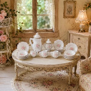 Op de afbeelding: Een miniatuur theeservies van wit porselein met delicate roze rozenpatronen. De set bevat een theepot, een suikerpot met deksel, een melkkannetje, meerdere kleine kopjes en bijpassende schoteltjes op een ronde, wit afgewerkte houten tafel.