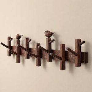 May include: A dark brown wooden wall-mounted coat rack featuring a horizontal base with multiple vertical pegs and two carved bird figures perched on top of two of the pegs. The rack has a smooth finish and a natural wood grain texture throughout.