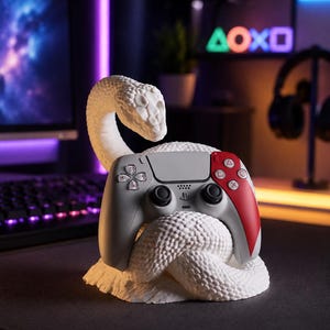 May include: A white 3D-printed snake sculpture coiled around a grey and red video game controller. The snake has a detailed scale texture and its head is raised above the controller. The controller features black analogue sticks and buttons.
