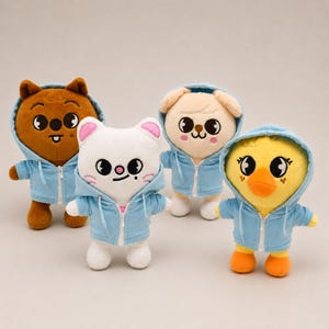 May include: Four plush animal toys, each wearing a light blue hooded sweatshirt with a white zipper. The characters include a brown bear, a white cat with pink ears, a beige puppy, and a yellow duck, all featuring large eyes and embroidered details.