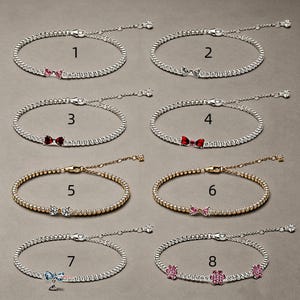 May include: Eight bracelets arranged in two columns, numbered one through eight. Each bracelet features a delicate chain with small metallic beads and a central charm, including various colored bows and flower shapes, set against a neutral background.