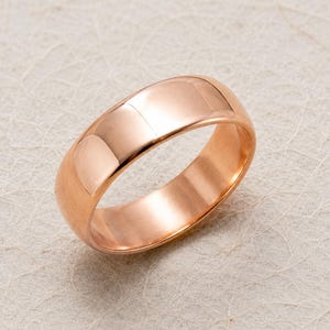 Può includere: Un anello a fascia in oro rosa lucido con una superficie esterna liscia e arrotondata di larghezza costante. Il metallo presenta una calda tonalità oro rosato con riflessi luminosi sulla parte superiore curva, dal design semplice e solido.