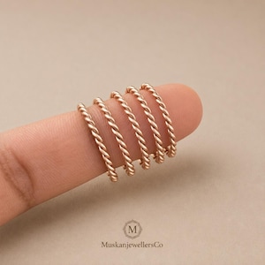 Peut inclure: Cinq bagues en or rose avec une texture en corde torsadée disposées en rangée. Chaque bague présente un motif en spirale continu. Les bagues sont présentées ensemble, mettant en valeur leur finition métallique et leur design uniforme. Le logo MuskanJewellersCo est visible.