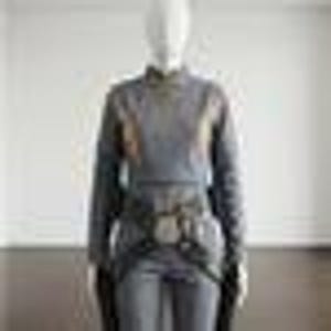 May include: A long-sleeved grey top featuring a high neckline and a textured, patterned fabric. The garment includes a dark, wide belt cinched at the waist with a prominent central buckle, paired with matching grey trousers in a solid, neutral tone.