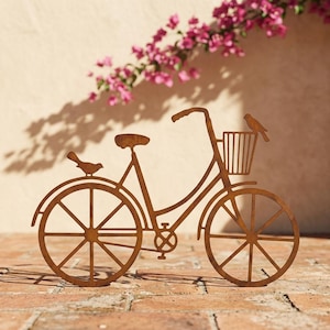 May include: A rust-coloured metal silhouette of a bicycle featuring a front basket and a seat. Two small bird figures are attached to the frame, one perched on the rear mudguard and another sitting on the edge of the front basket, creating a decorative piece.
