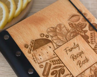 Peut inclure: Un livre de recettes en bois avec une reliure noire et un élastique, orné de gravures laser représentant du fromage, des pâtes et des herbes. La couverture porte le texte Family Recipe Book dans une police cursive sur le bois veiné.