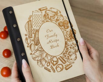 Peut inclure: Un livre de recettes en bois avec une reliure en cuir noir fixée par quatre rivets métalliques. La couverture présente un ovale central avec le texte "Our Family Recipe Book" entouré de gravures laser de pâtes et de tomates.