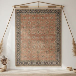 May include: A rectangular area rug featuring a terracotta orange field with a repeating floral medallion pattern in muted green and cream, enclosed by a dark blue border with intricate vine motifs and finished with short fringe at the bottom.
