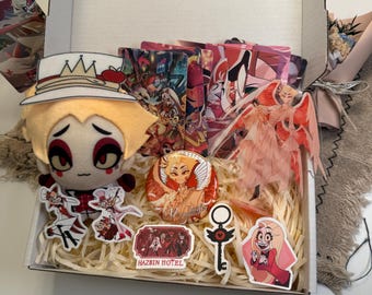 May include: A gift box containing a plush character doll with a white top hat, several rectangular character cards, a circular pinback button, a translucent acrylic figure, and various die-cut stickers featuring Hazbin Hotel imagery.