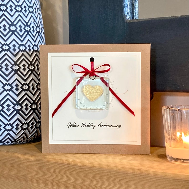 May include: A card with a gold heart inside a clear square, tied with a red ribbon. The card says "Golden Wedding Anniversary".
