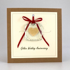 May include: A card with a red ribbon tied around a square glass ornament with a gold heart inside. The card has the text "Golden Wedding Anniversary" printed on it.