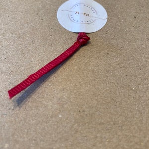 May include: A white circle tag with the text "Mini Wafer Fused Glass" and the number "11.70" in gold lettering. A red ribbon is attached to the tag.