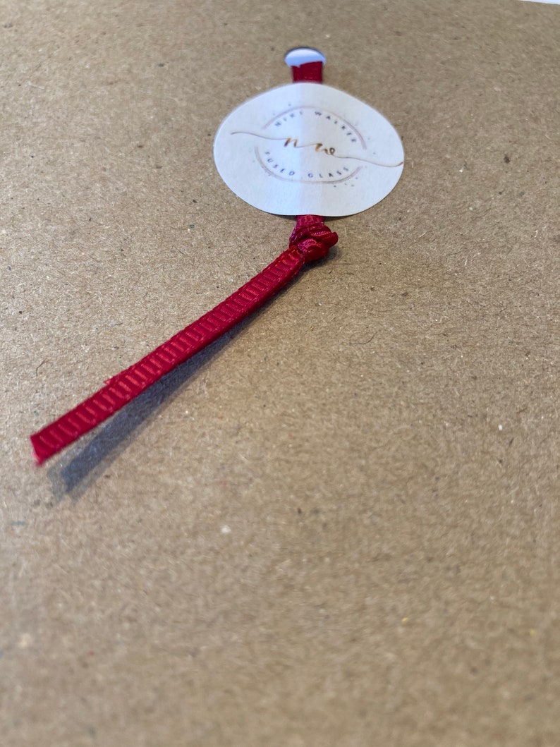 May include: A white circle tag with the text "Mini Wafer Fused Glass" and the number "11.70" in gold lettering. A red ribbon is attached to the tag.
