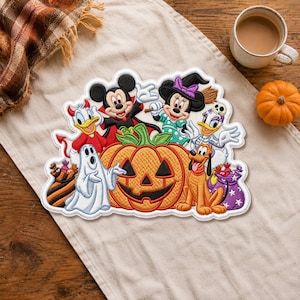 Może przedstawiać: Haftowana naszywka przedstawiająca postacie Disneya w kostiumach na Halloween, w tym Myszkę Miki jako wampira, Minnie jako czarownicę, Kaczora Donalda jako diabła, Daisy jako szkielet oraz Pluto, otaczających dużą pomarańczową dynię z wyciętą twarzą.
