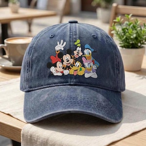 Può includere: Un cappellino da baseball in denim blu scuro con una stampa grafica colorata di Topolino, Minni, Pippo, Pluto, Paperino e Paperina. Il cappellino presenta una visiera curva, una corona strutturata e un classico design a sei pannelli.