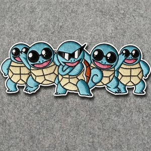 May include: An embroidered patch featuring five light blue turtle-like creatures with tan shells. Each character has a distinct pose and wears black sunglasses, with the central figure wearing angular, pointed shades while the others wear round ones.