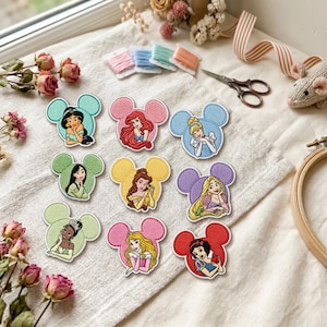 May include: Nine embroidered patches featuring various animated princesses, each framed within a Mickey Mouse-shaped silhouette. The patches display characters with distinct hair and clothing colors, including teal, pink, blue, green, yellow, purple, light green, magenta, and red backgrounds.