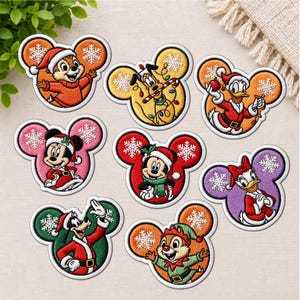 Può includere: Una collezione di otto toppe ricamate termoadesive con personaggi Disney in abiti festivi, ciascuna incorniciata in una silhouette a orecchie di Topolino. I disegni includono fiocchi di neve e colori festosi come rosso, verde, arancione e viola.