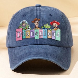May include: A navy blue baseball cap featuring a graphic print of Buzz Lightyear, Woody, an alien, and Jessie from Toy Story above the word Disneyland. The text is displayed in a colourful, block-letter style with each letter on a separate rectangle.