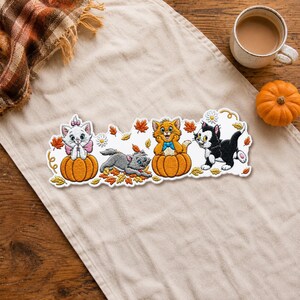 Peut inclure: Un écusson décoratif représentant quatre chatons dans un décor automnal. Un chaton blanc avec un nœud rose est assis dans une citrouille, un chaton gris joue dans des feuilles orange, un chaton orange avec un nœud bleu est dans une citrouille.
