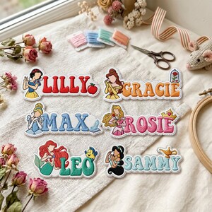 Pode incluir: Seis emblemas bordados com nomes, personagens de desenhos animados e ícones. Os emblemas exibem os nomes LILLY, GRACIE, MAX, ROSIE, LEO e SAMMY em várias cores, cada um acompanhado por uma ilustração de personagem e um pequeno símbolo.