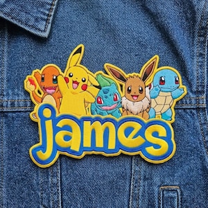 May include: An embroidered patch featuring the characters Charmander, Pikachu, Bulbasaur, Eevee, and Squirtle positioned above the name James in yellow lettering with a blue outline, all stitched onto a blue denim fabric background.