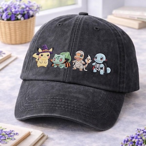Può includere: Un cappellino da baseball grigio antracite con un ricamo raffigurante quattro personaggi dei cartoni animati in costume di Halloween: un personaggio giallo con cappello da strega viola, uno verde con mantello, uno arancione bendato e uno blu.