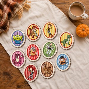 May include: A collection of ten oval-shaped embroidered patches featuring various cartoon characters from the Toy Story franchise, each set against a striped background with a scalloped border, arranged in a cluster on a light-colored fabric surface.