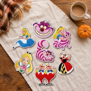 Op de afbeelding: Een verzameling van zeven geborduurde patches met personages uit Alice in Wonderland, waaronder Alice, de Cheshire Cat, de Hartenkoningin en Tweedle Dee en Tweedle Dum, allemaal uitgevoerd in levendige kleuren met gedetailleerd stikwerk.