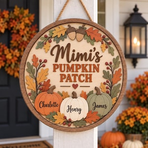 May include: A round wooden door sign featuring the text Mimi's PUMPKIN PATCH with a small heart. The design includes three dimensional pumpkins labeled Charlotte, Henry, and James, surrounded by autumn leaves, berries, and two acorns.