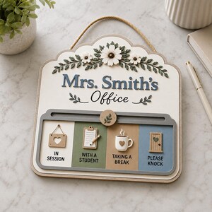 May include: A white wall sign with a rope hanger featuring the text Mrs. Smith's Office and a floral design. Below, a sliding mechanism displays four status options: In Session, With a Student, Taking a Break, and Please Knock, each with an icon.