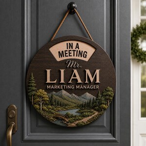 May include: A round dark wood door sign hanging by a rope. The sign features the text IN A MEETING, Mr. LIAM, and MARKETING MANAGER. Below the text is a detailed landscape illustration of mountains, a river, a small bridge, and pine trees.