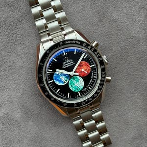 Op de afbeelding: Een roestvrijstalen Omega Speedmaster Professional chronograaf horloge met een zwarte wijzerplaat. De wijzerplaat bevat drie sub-wijzerplaten met Mars, de aarde en de maan, met de tekst "FROM THE MOON TO MARS" aan de rechterkant gedrukt.