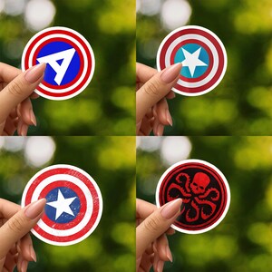 May include: A set of four circular vinyl stickers featuring iconic shield designs. One displays a white letter A on a blue and red background, another a white star on a blue and red shield, a distressed red and blue shield, and a red skull with tentacles.