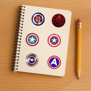 May include: A spiral-bound notebook featuring six circular stickers. The stickers display various designs including a Union Jack shield, a red Hydra skull emblem, three different red, white, and blue star shields, and a blue letter A on a shield.