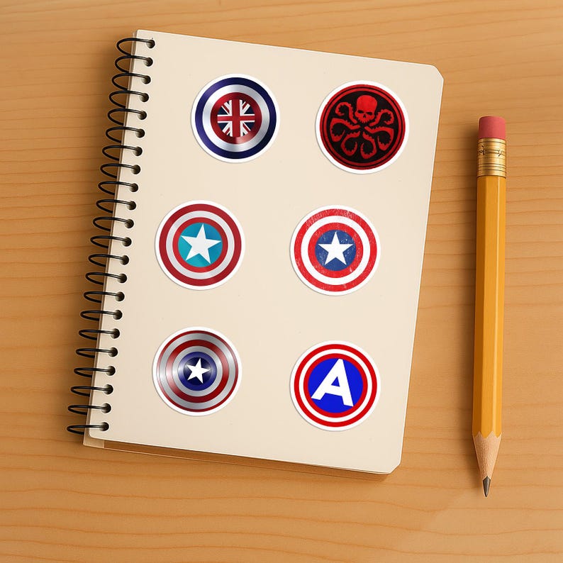 May include: A spiral-bound notebook featuring six circular stickers. The stickers display various designs including a Union Jack shield, a red Hydra skull emblem, three different red, white, and blue star shields, and a blue letter A on a shield.