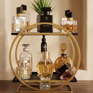 May include: A two-tiered circular gold metal display stand with black shelves holding various glass perfume bottles of different shapes and sizes, including a black bottle labeled Duchess and a gold round bottle, plus a small green potted plant.