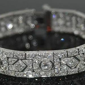 May include: A silver-toned metal bracelet featuring a repeating pattern of circular and geometric links. The entire surface is encrusted with numerous small, clear, sparkling stones, creating a highly reflective and textured appearance throughout.