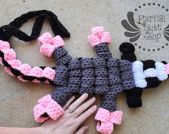 May include: A crocheted black, white, and pink scorpion with a long tail. The scorpion has a segmented body and a stinger at the end of its tail.