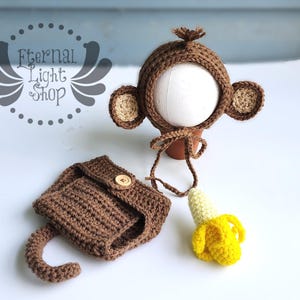 Puede incluir: Un conjunto de ganchillo marrón con un gorro de mono con orejas, una braguita y un plátano amarillo. El conjunto está diseñado para un bebé o un niño pequeño.