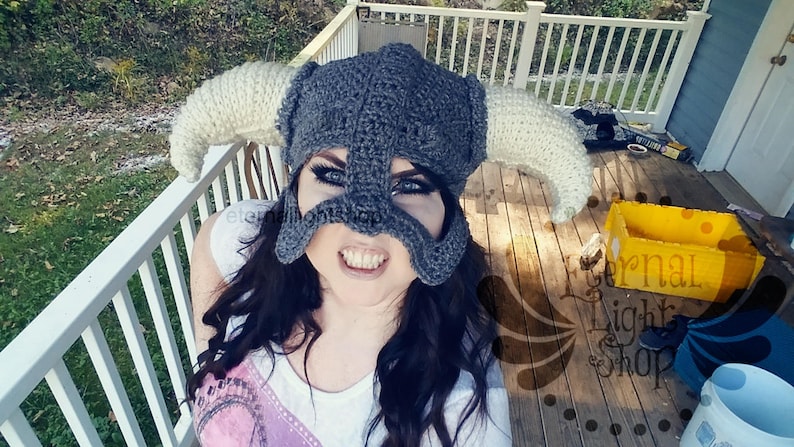 Puede incluir: Primer plano de una persona que lleva un casco de ganchillo gris con cuernos blancos. El casco tiene una m&aacute;scara facial con agujeros para los ojos y una expresi&oacute;n feroz. La persona sonr&iacute;e y mira directamente a la c&aacute;mara.