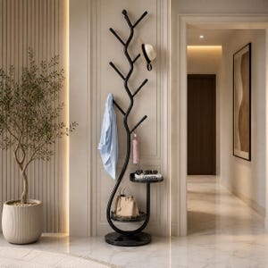 May include: A black metal coat rack shaped like a tree with multiple branches for hanging items. It features two circular marble shelves, a light blue shirt, a white hat, a small pink umbrella, a beige handbag, and a book labelled CHANEL.