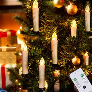 May include: A set of battery-operated LED taper candles with a cream-colored wax-like finish and warm glowing flame tips, attached to green pine branches, accompanied by a white remote control featuring buttons labeled ON, OFF, 6H, SL, FL, +, and -.