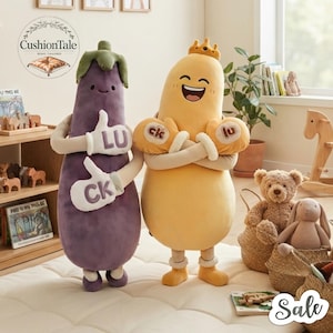 May include: Two plush toys, one purple eggplant-shaped figure with green leaves on top and one yellow pear-shaped figure wearing a small crown. Both figures have arms with white gloves featuring the letters LU and CK, and simple facial expressions.