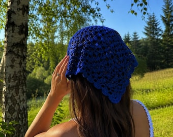 May include: A vibrant royal blue crochet headscarf featuring an intricate openwork pattern with a scalloped edge. The triangular-shaped accessory is crafted from yarn and displays a detailed, repeating stitch design throughout the fabric.