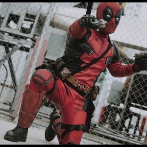 May include: A red and black tactical bodysuit featuring a full-face mask with white eye patches, black gloves, a utility belt with pouches, knee pads, and shin guards. The figure is in a kneeling pose, holding two handguns pointed forward.